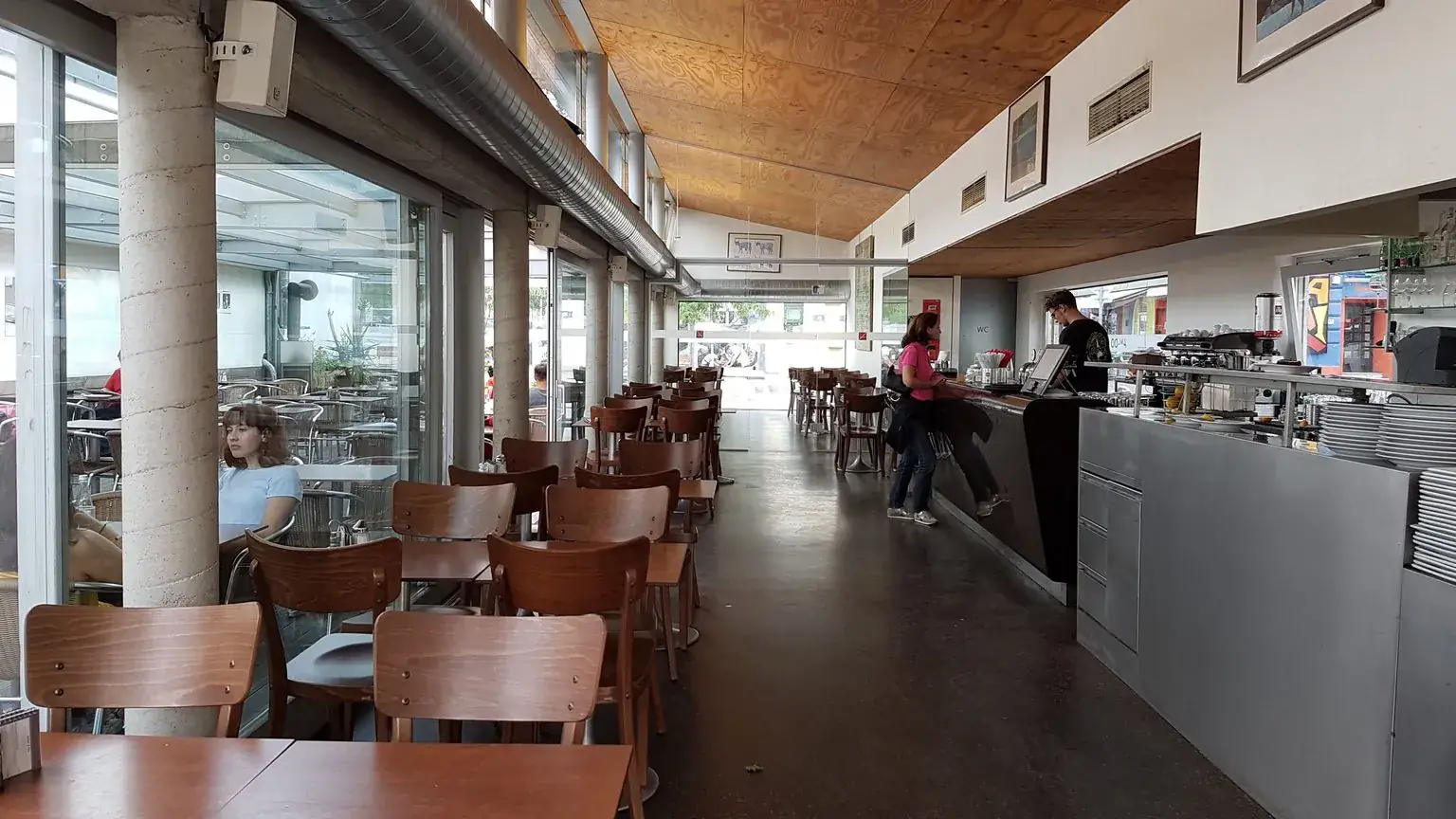 Sonnendurchflutetes Innere des Café AnDo mit Holzstühlen, Pflanzen und großen Fenstern