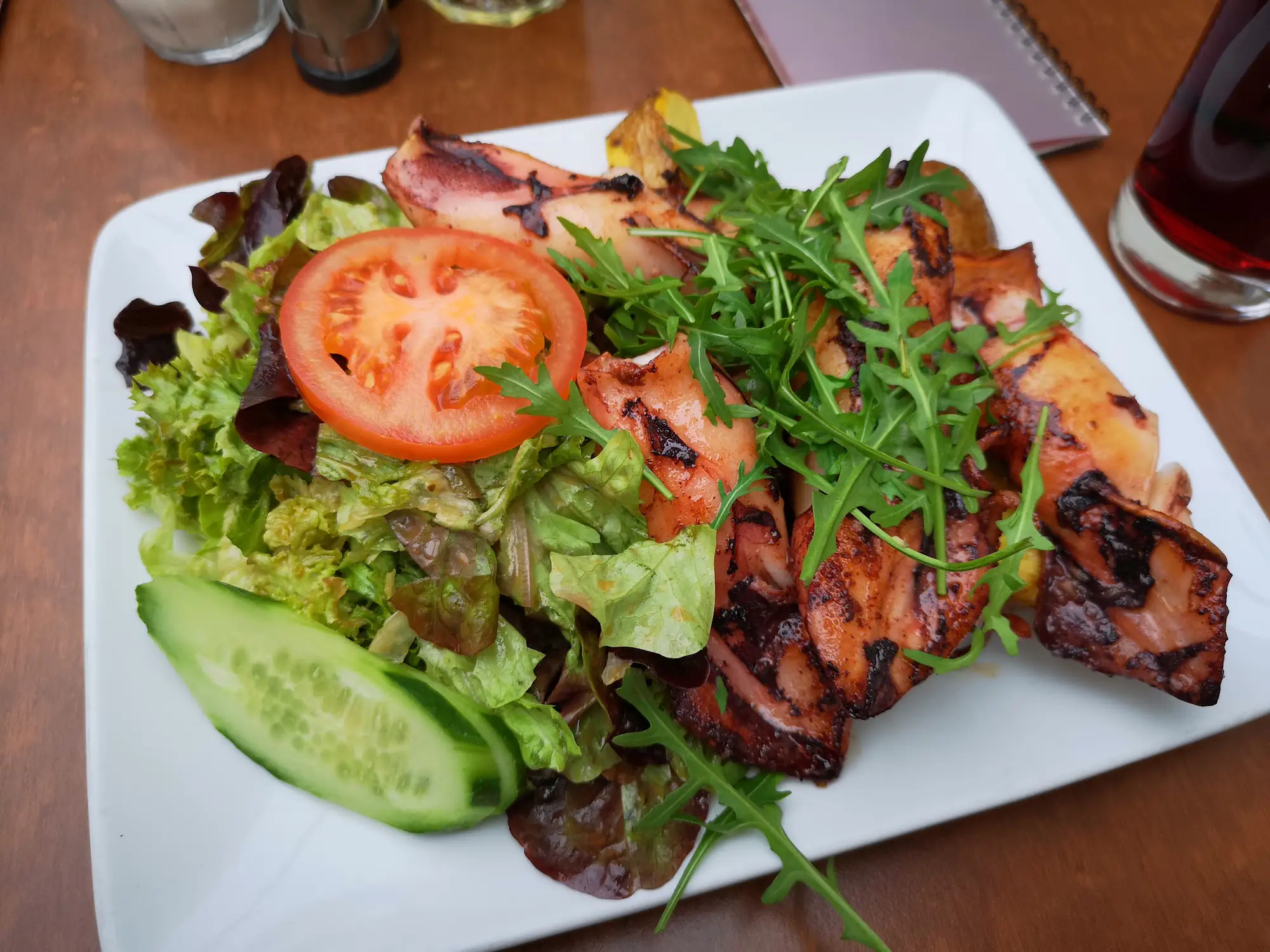 Gegrillte Calamari mit Rucola, Salat, Gurke und Tomate auf weißem Teller