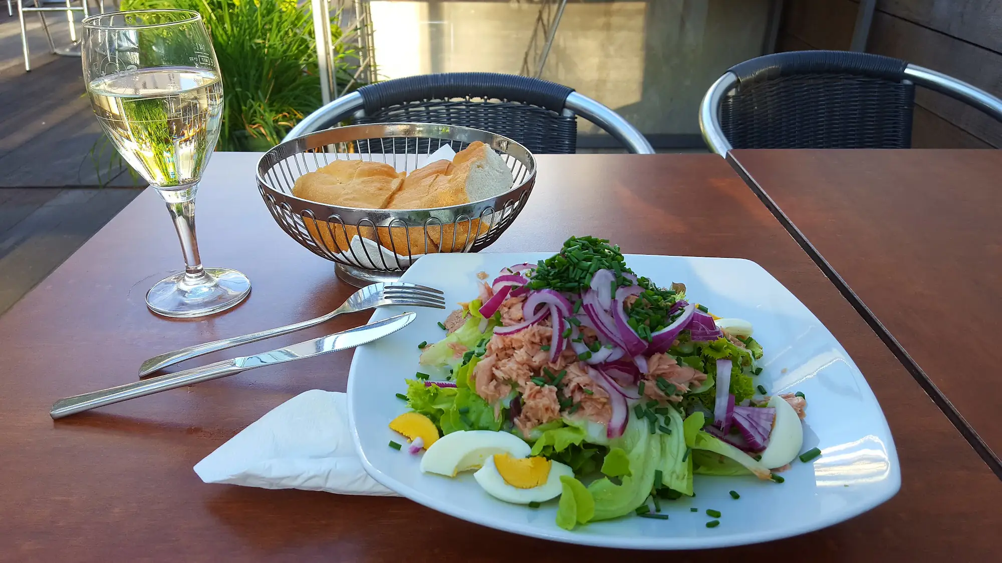 Gedeckter Terrassentisch mit Thunfischsalat, Brotkorb und einem Glas Weißwein